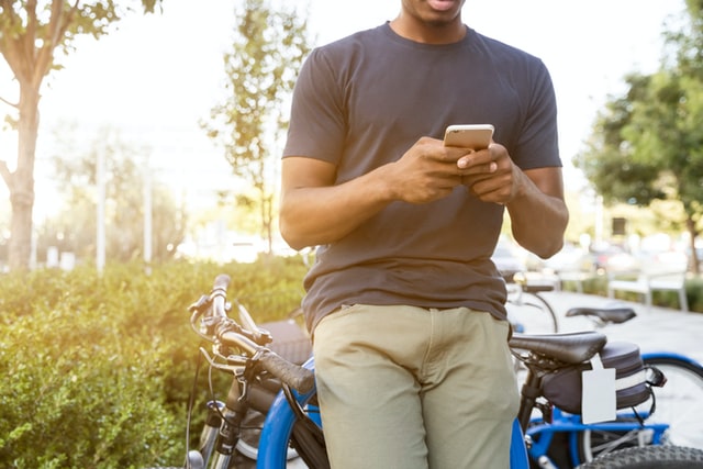 На изображении мужчина, сидящий на велосипеде со своим телефоном в руках и переписывающийся.