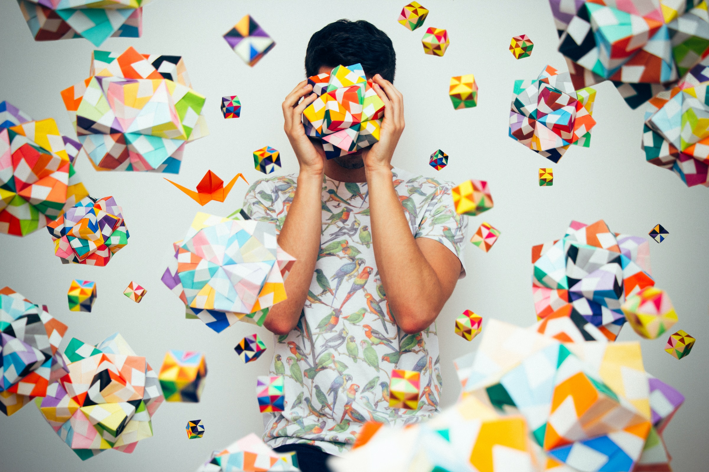 There are a lot of colourful cubes on a gray background. In the centre there is a man standing and closing his eyes with his hands and a colourful figure like a