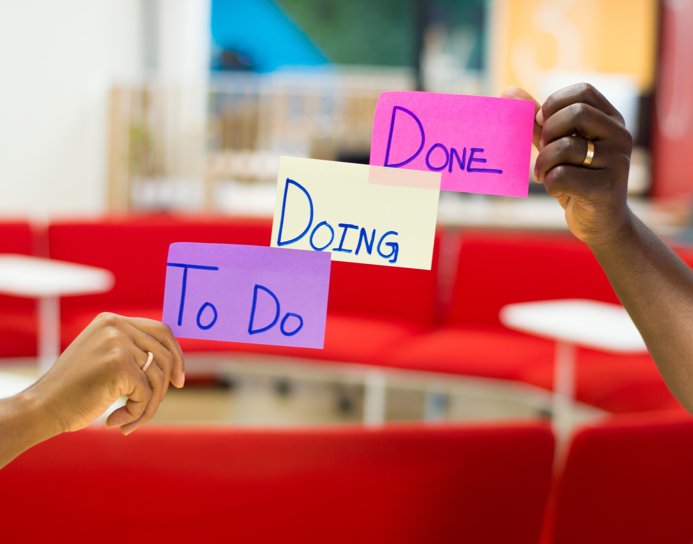 There are two people showing three sheets of paper. On these sheets are written “to do”, “doing”, “done”.